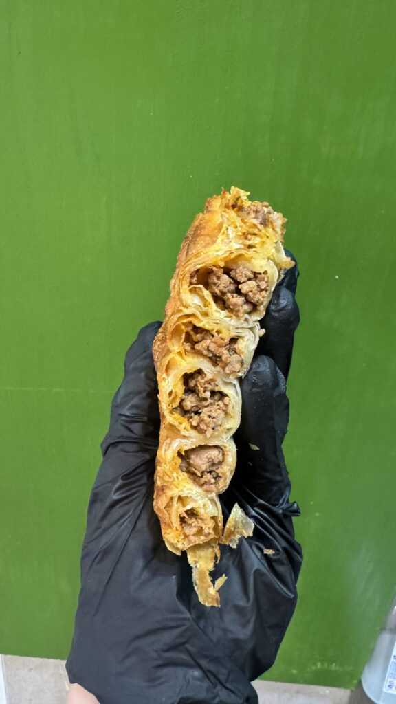 Porción de burek/börek en espiral de carne sujeta con la mano